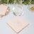 Glass of water on a pink napkin with gold trim, styled with decorative elements.