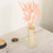 Pink dried flowers in a glass vase on a wooden table.