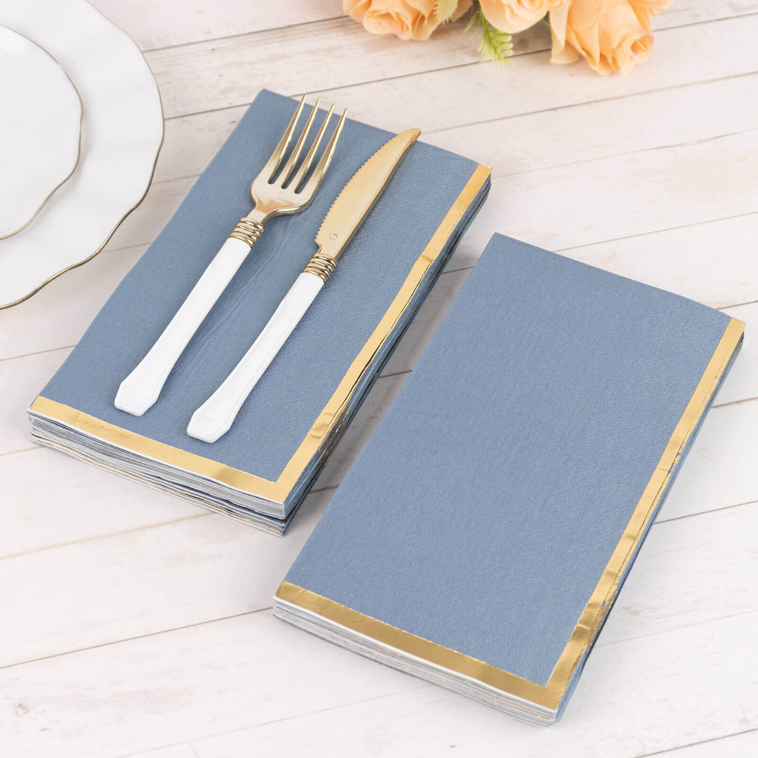 Blue napkins with gold trim and white cutlery on a wooden table.