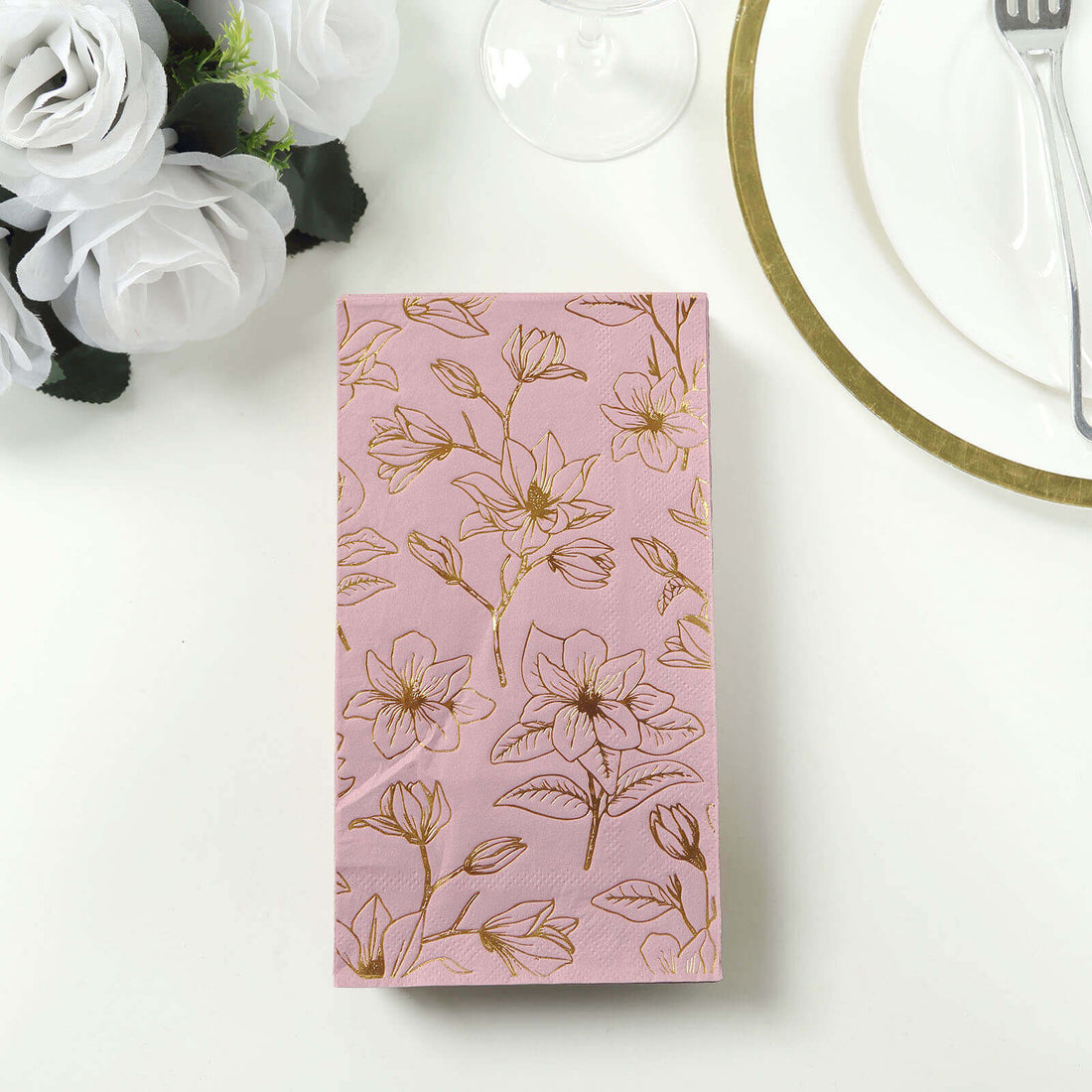 Floral-patterned pink gift box on a table with white roses and dinnerware.