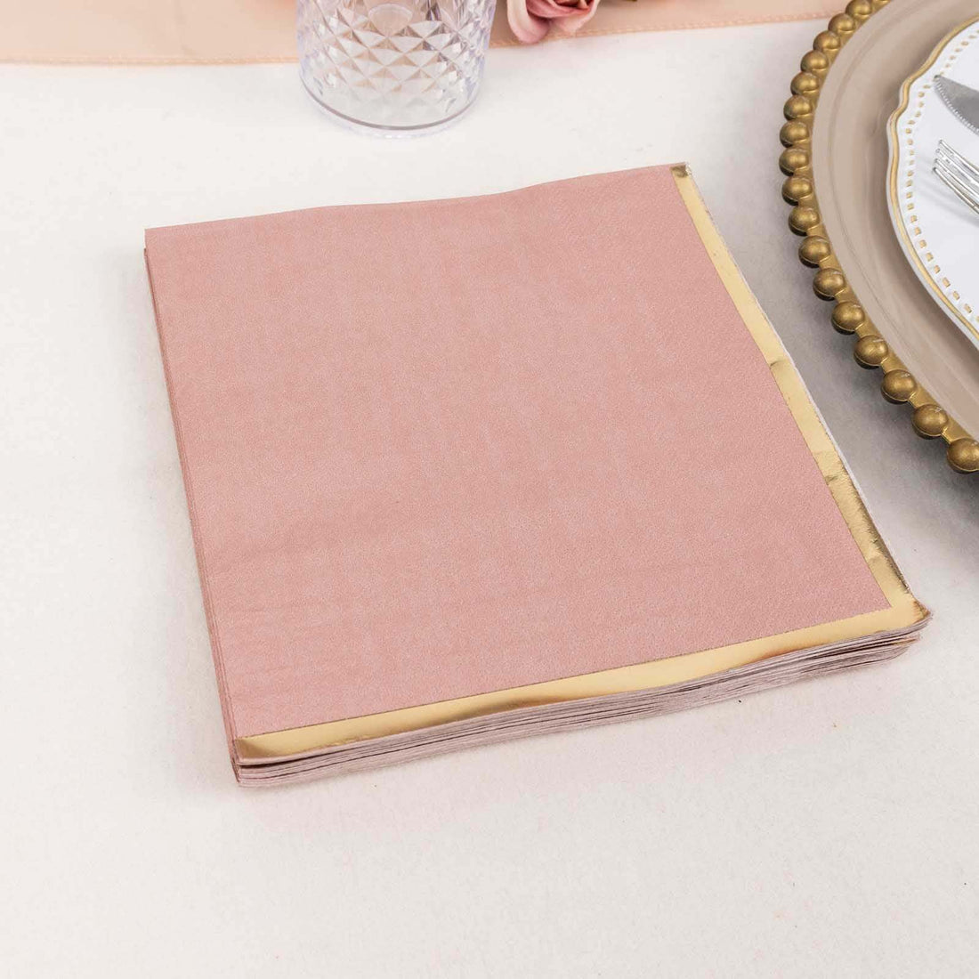 Pink napkins with gold trim stacked neatly on a table.