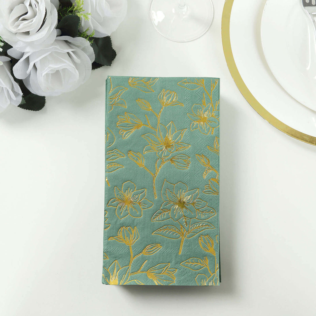 Decorative teal napkin with gold floral pattern on a dining table.