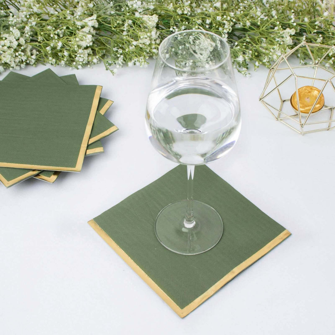 Green napkin with gold trim under a glass of water, surrounded by decorative elements.