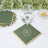 Green napkin with gold trim under a glass of water, surrounded by decorative elements.