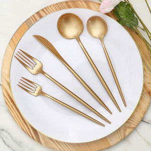 Gold cutlery set on a white plate with a wooden serving board.