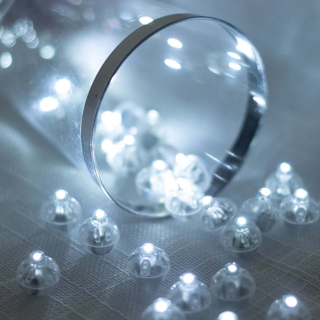 LED light bulbs in a clear cup with scattered bulbs on a soft surface.