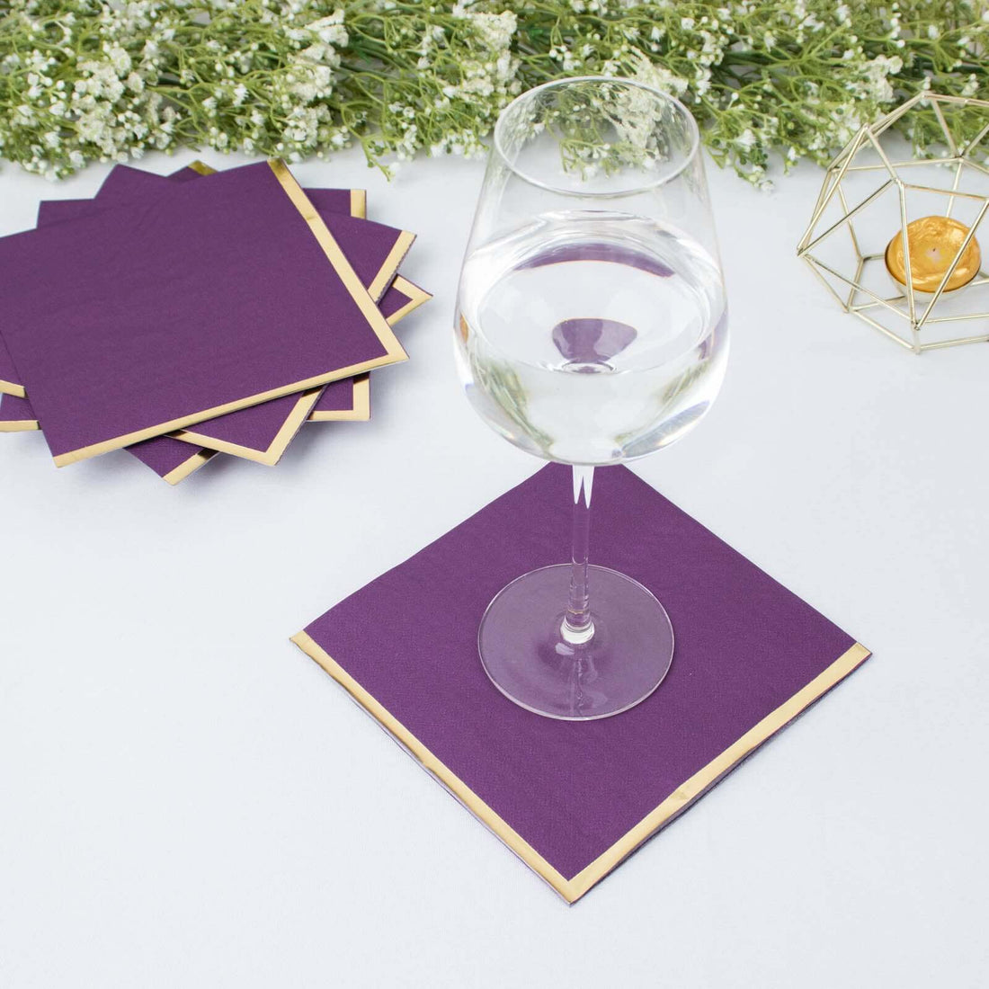 Purple coasters with gold trim under a glass of water on a table.