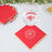 Red napkins with gold trim under a glass of water on a table.