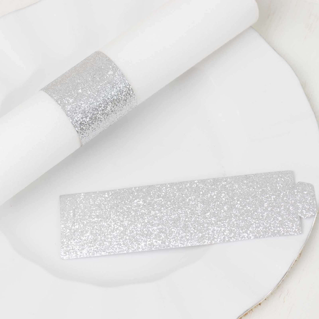 Silver glitter napkin ring and place card on a white plate.