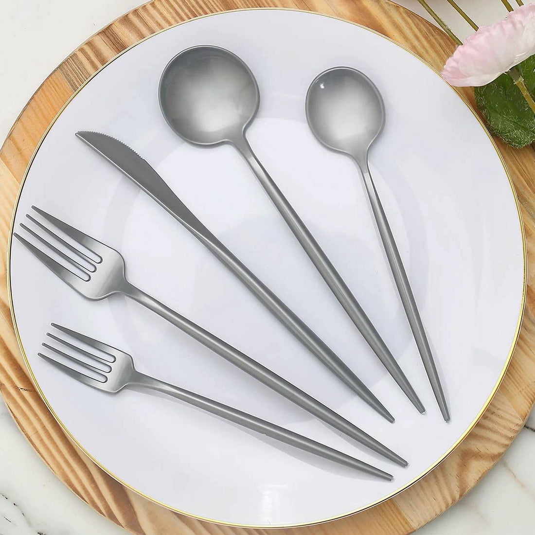 Gray cutlery set on a white plate with wooden serving board.