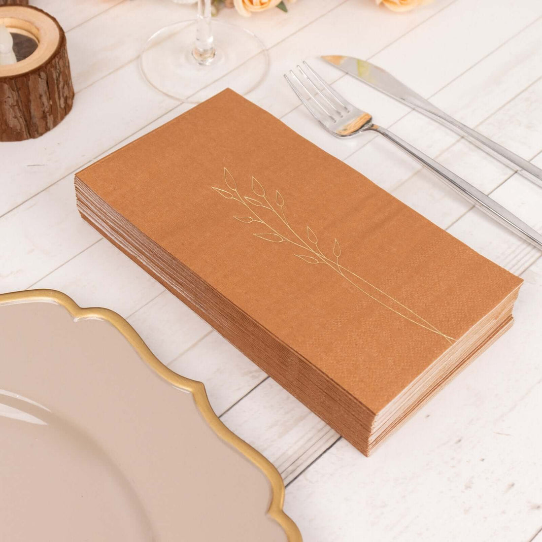 Elegant brown napkin set with gold leaf design on a rustic table setting.