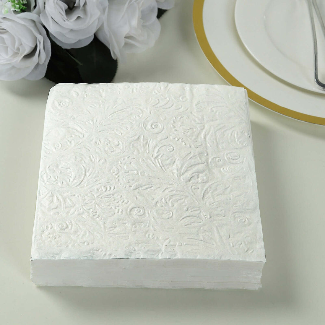 White embossed napkins stacked on a table with floral decor.