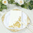 Elegant white napkin with gold floral design on decorative plate with utensils.