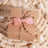 Brown gift box with pink bow on woven surface.