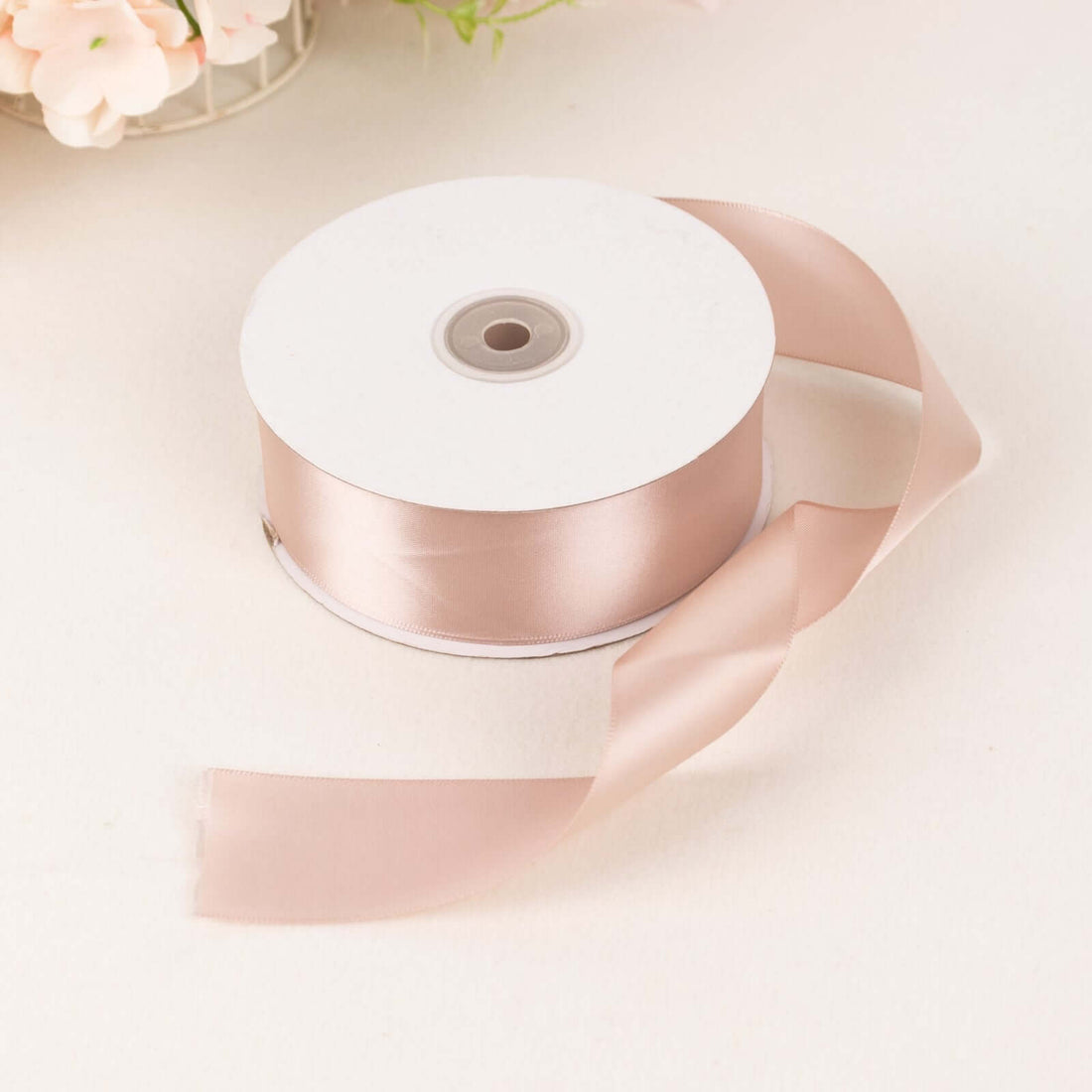 Pink satin ribbon on a spool with a loose end, perfect for crafting and decorating.