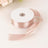 Pink satin ribbon on a spool with a loose end, perfect for crafting and decorating.