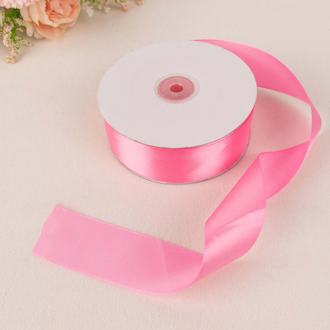 Pink satin ribbon roll on a light surface with a floral background.
