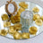 Glass candle holder surrounded by gold rose petals on a mirrored surface.
