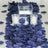 Navy blue rose petals scattered on a table with glass candle holders and a vase.