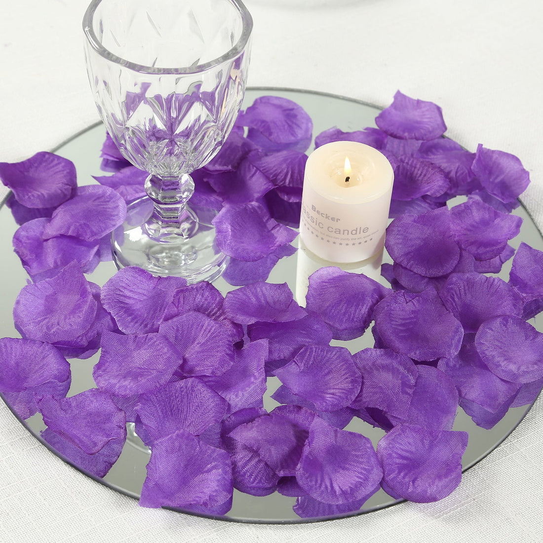 Purple silk rose petals with a candle and glass on a mirrored tray.