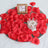 Red rose petals scattered on a mirror tray with a candle and a framed note.