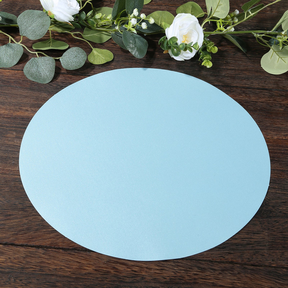 Blue circular backdrop on a wooden surface with greenery and white flowers.