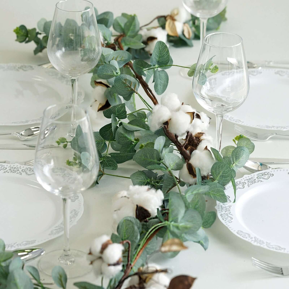 Elegant table setting with cotton and greenery centerpiece.