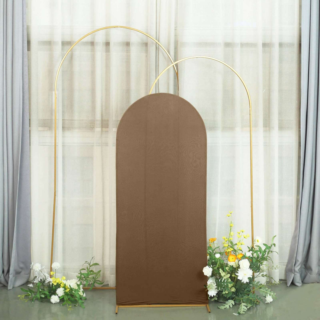 Brown backdrop with gold arch and floral arrangement in soft interior setting.