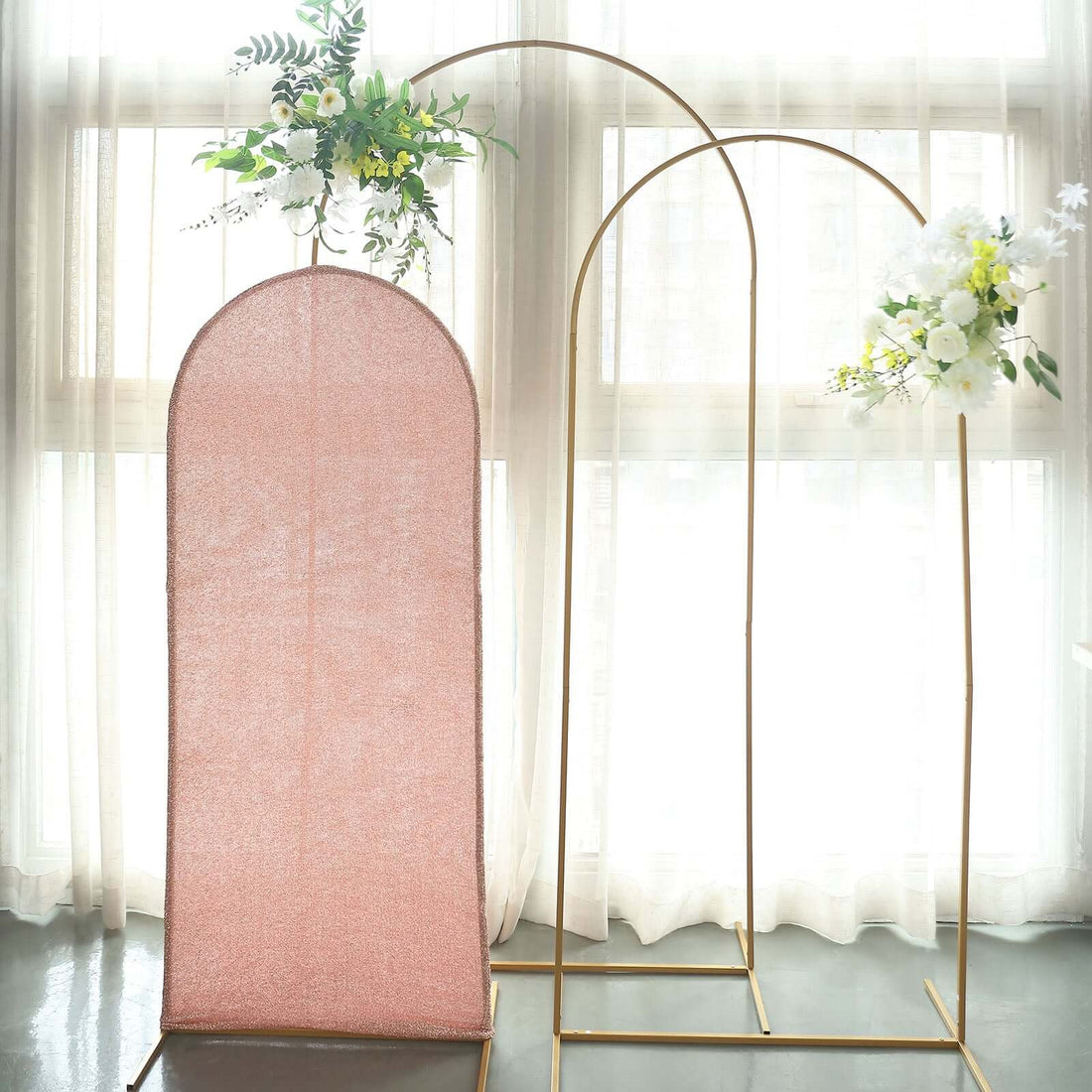 Pink backdrop with gold stand and floral arrangements in a bright, airy setting.