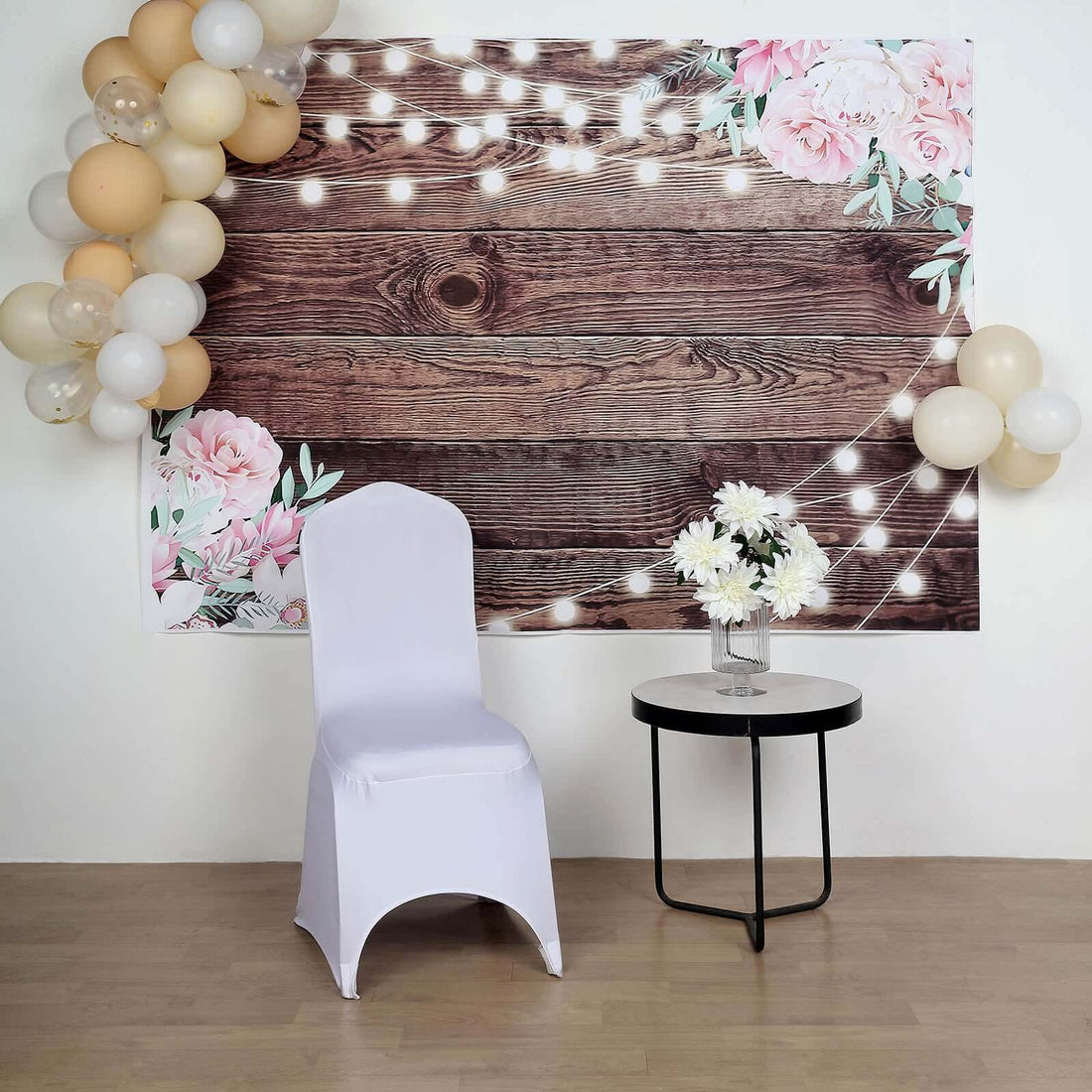 White chair with a floral backdrop and decorative balloons at an event setup.