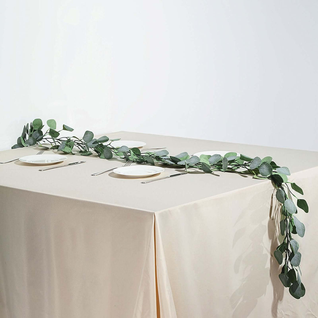 Eucalyptus table runner on beige table with plates and cutlery.