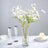 White daisies in a glass vase on a table with champagne flutes and candles.