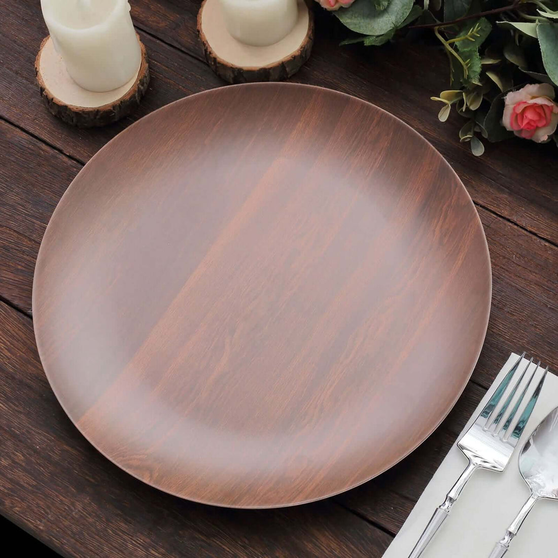 Brown wooden dinner plate on a rustic table with candles and greenery.
