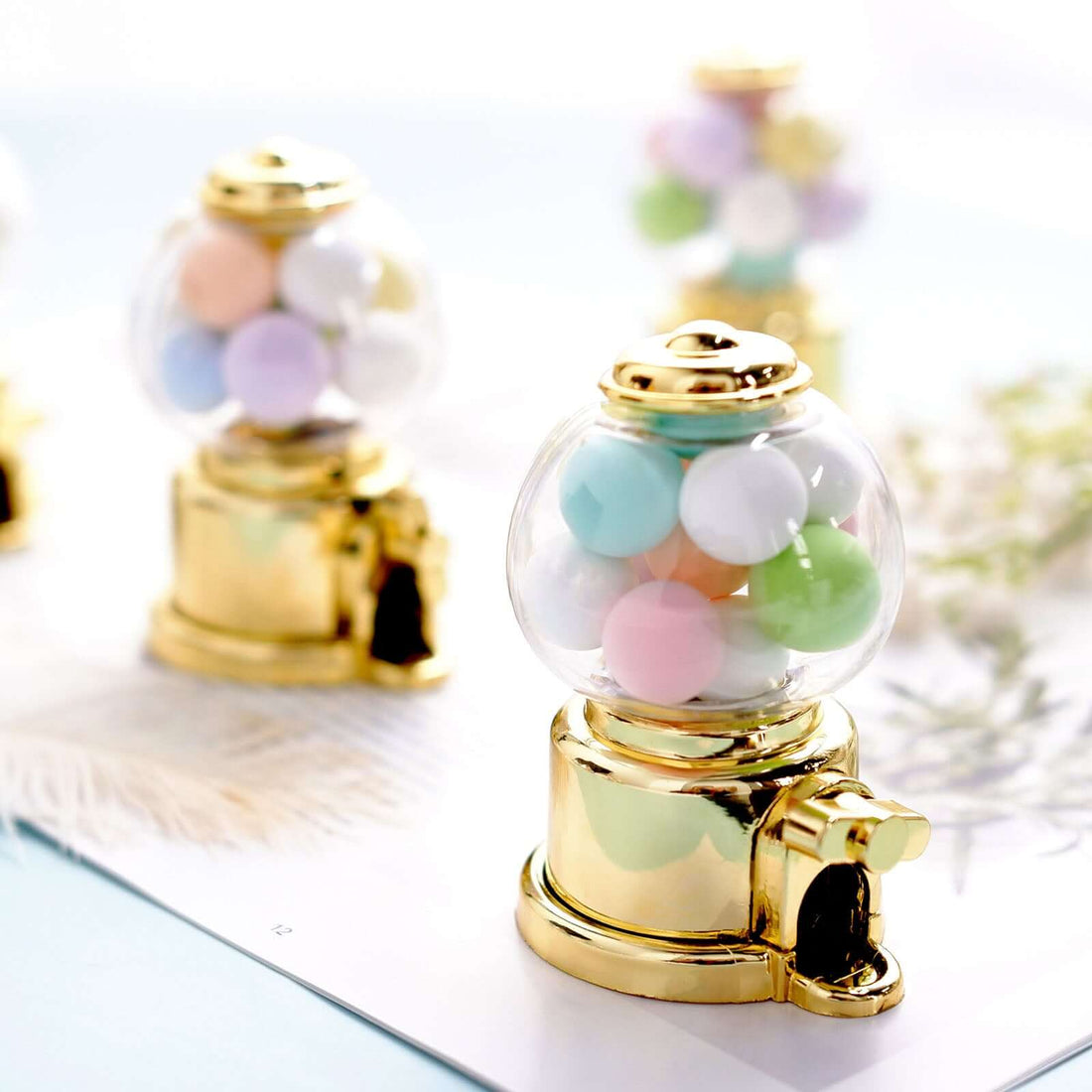 Miniature golden gumball machines filled with pastel gumballs.