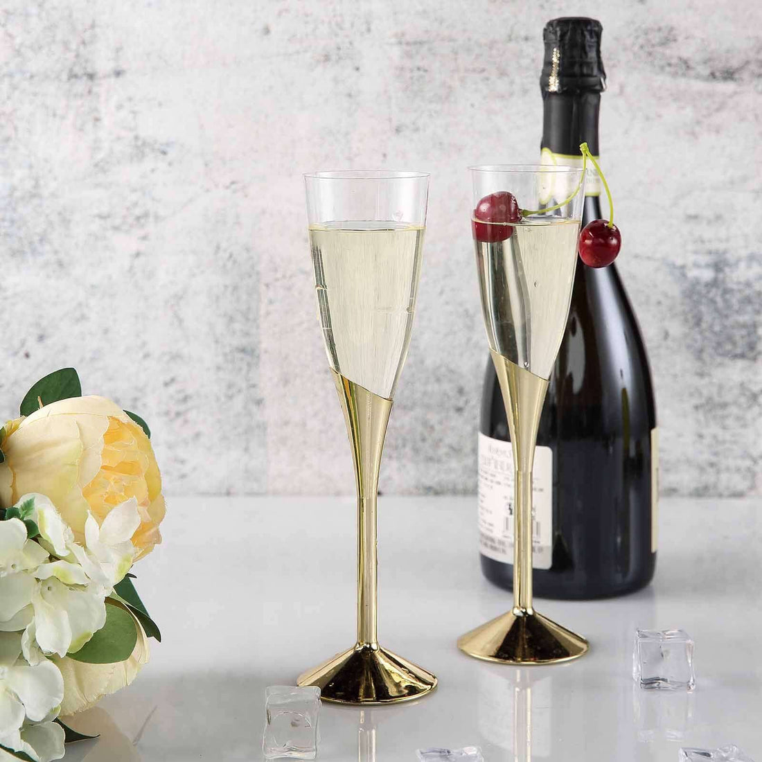Elegant champagne flutes with gold accents beside a bottle of bubbly and flowers.