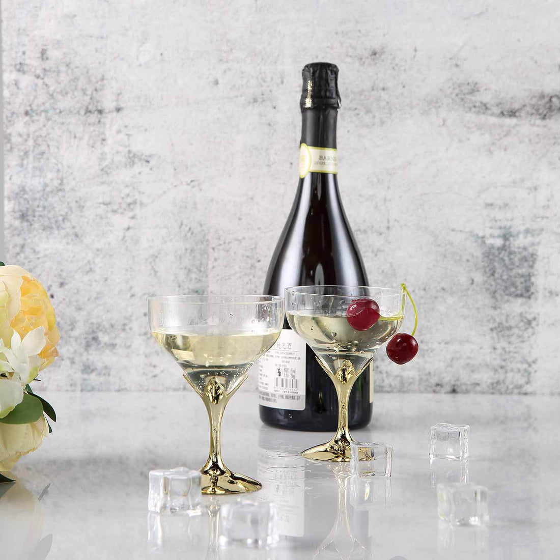 Elegant champagne glasses with cherries and a bottle of sparkling wine on a marble surface.