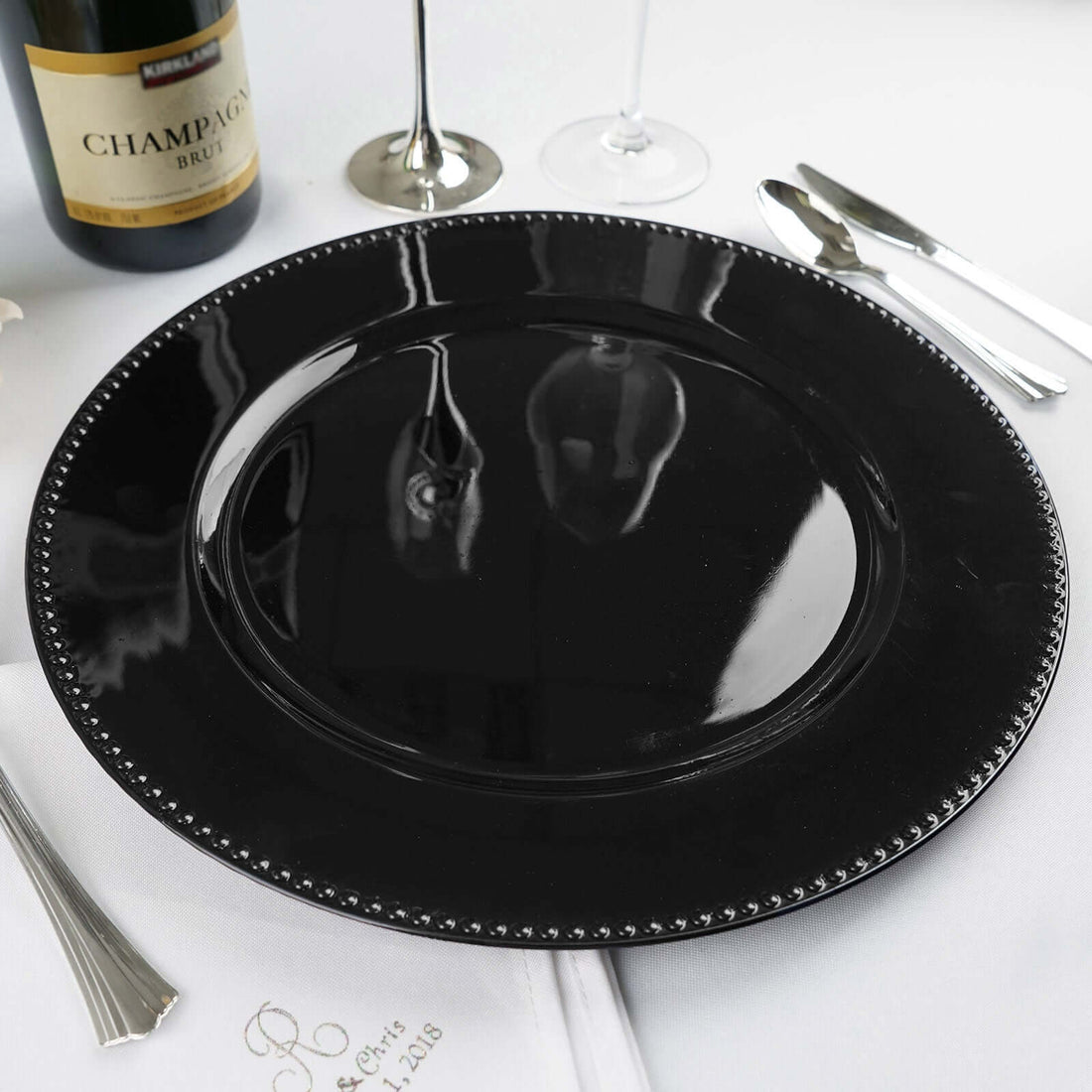 Black charger plate with beaded rim on a white table setting.