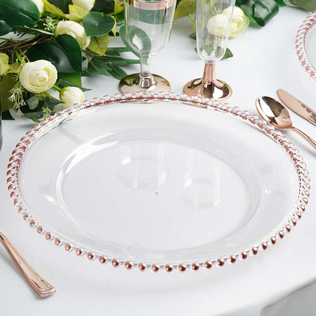 Clear glass charger plate with rose gold beaded rim on a dining table setting.