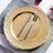 Gold decorative plate with knife and fork on a textured tablecloth.