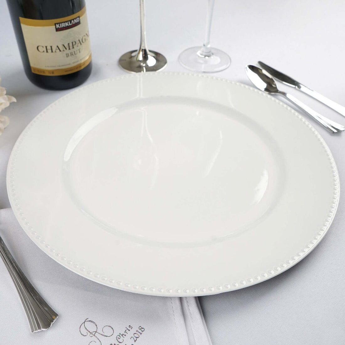 White decorative plate on a dining table with champagne and silverware
