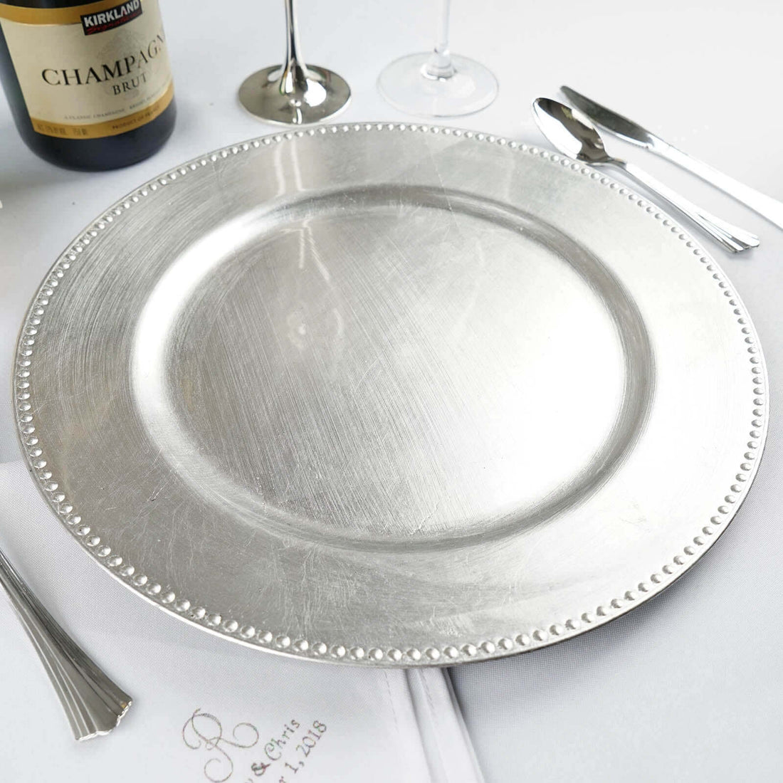 Silver charger plate on a dining table with wine and glassware.