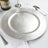 Silver charger plate on a dining table with wine and glassware.