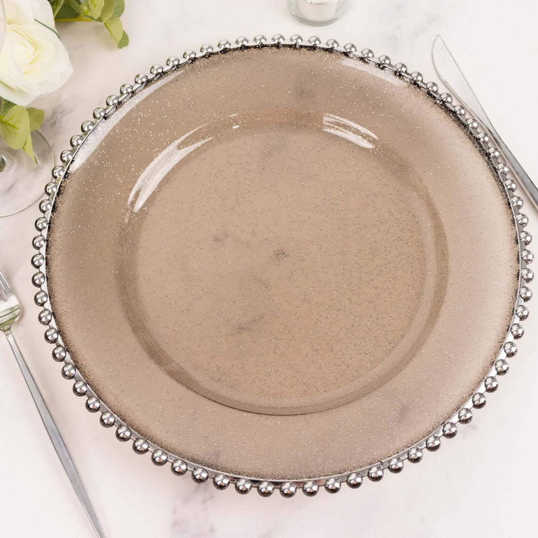 Elegant glass charger plate with beaded rim on a neutral background.