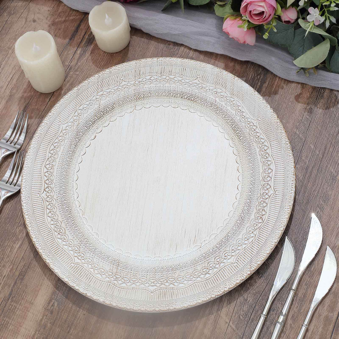 Decorative white serving platter on a wooden table with candles and flowers.