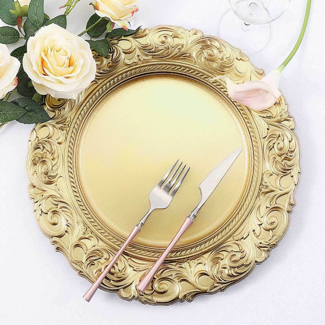 Elegant gold charger plate with ornate design, fork, and knife on a floral table setting.
