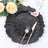 Black textured decorative plate with silver cutlery and floral accents.