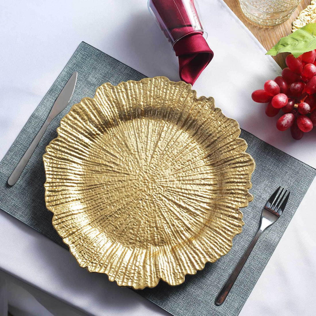 Gold textured serving platter on a table setting with utensils and grapes.