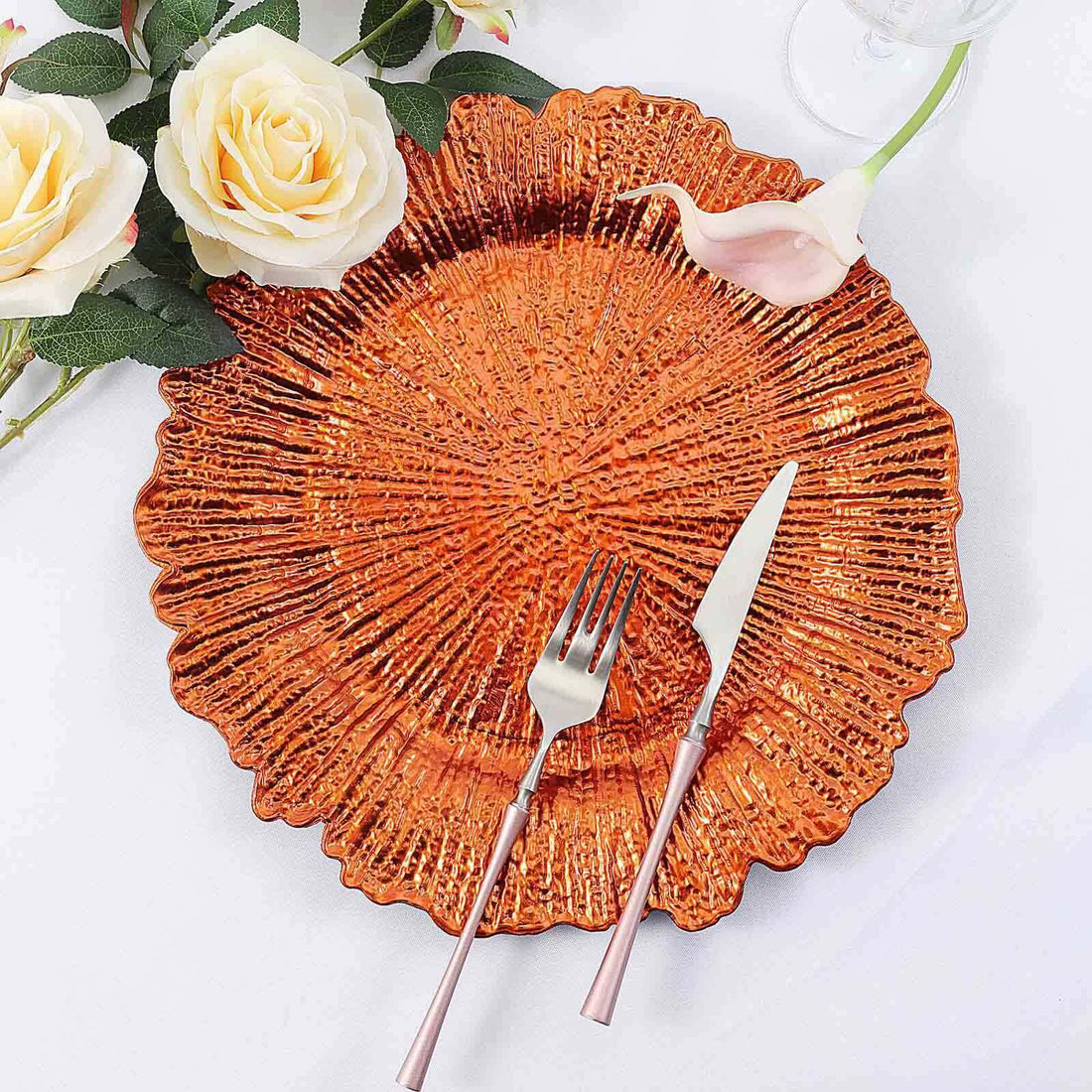 Orange decorative plate with rose gold cutlery and flowers on the side.
