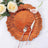 Orange decorative plate with rose gold cutlery and flowers on the side.