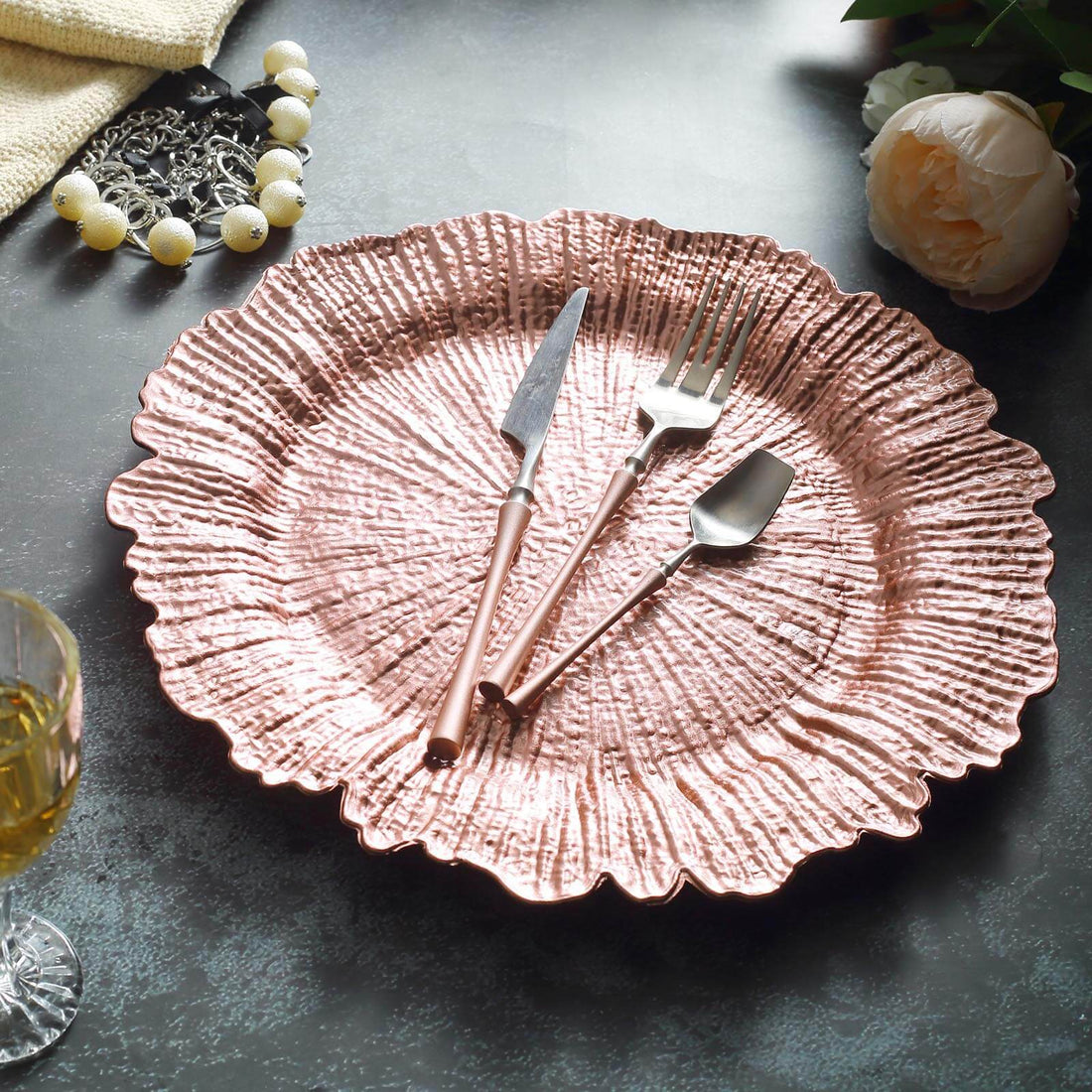 Rose gold decorative plate with cutlery on a textured surface.
